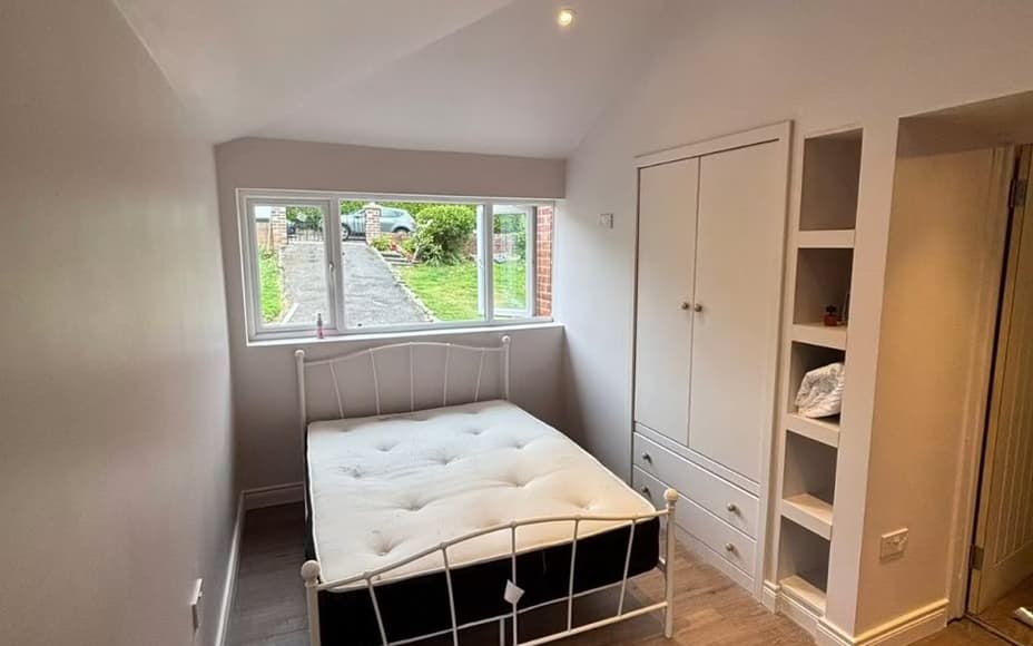 Garage converted into a bedroom by SMM — built-in wardrobe and shelving beside a wide window